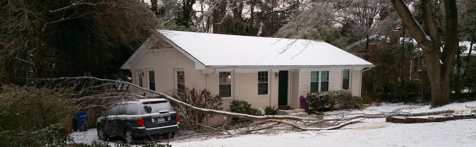 snow covered house with fallen tree